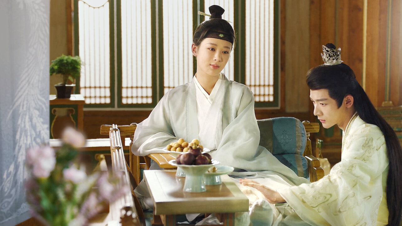 Cảnh phim Trường Tương Tư – Phần 1 với hình ảnh nữ chính trong nam trang và nam chính ngồi bên bàn trà trong không gian cổ trang yên tĩnh.