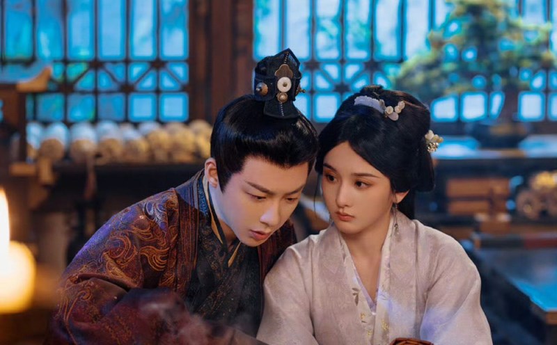 Cảnh phim Khom Lưng – The Prisoner of Beauty với hình ảnh nam – nữ chính ngồi cạnh nhau trong không gian cổ trang, chăm chú trao đổi công việc.